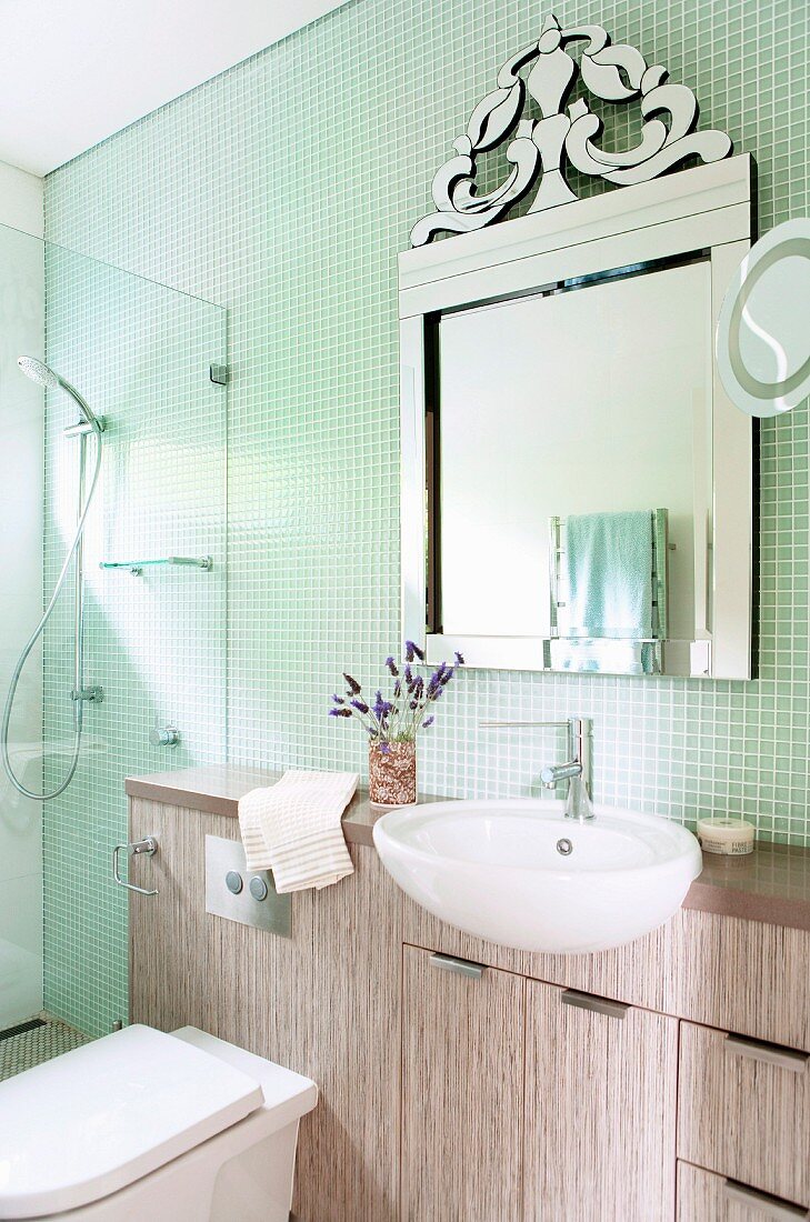 Washstand with protruding sink below ornate mirror on wall with mosaic tiles; glazed shower area in corner