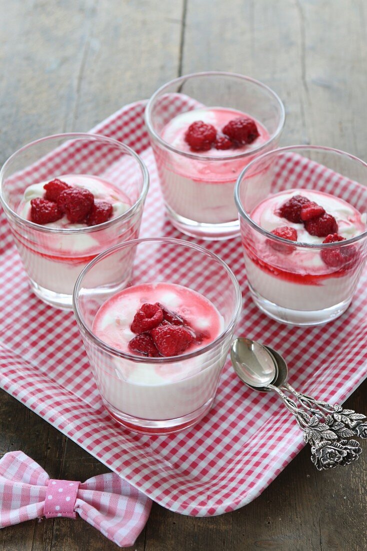 Glasses of vanilla yoghurt and raspberries on gingham tray