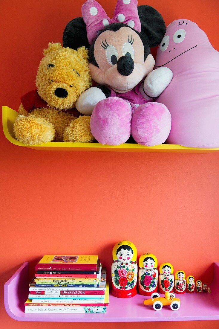 Soft toys and books on colourful shelves on orange wall