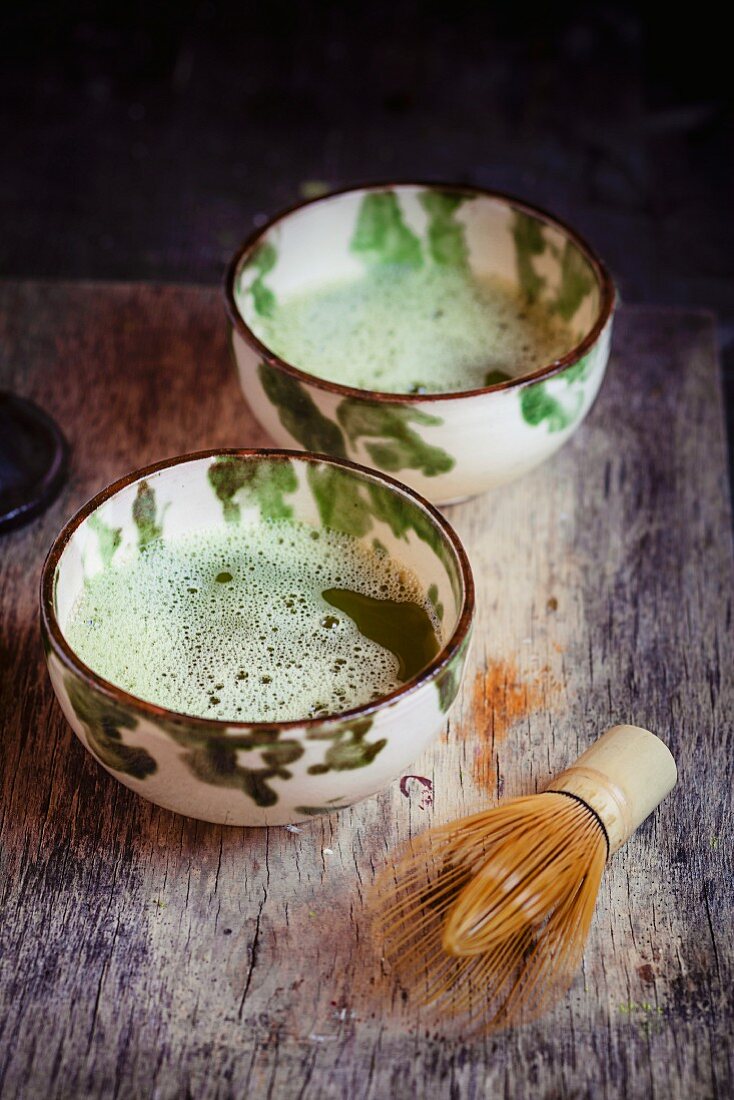 Bowls of matcha tea with a bamboo whisk