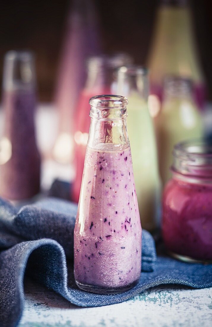 A blueberry smoothie in a bottle with other bottles of fruit smoothies in the background