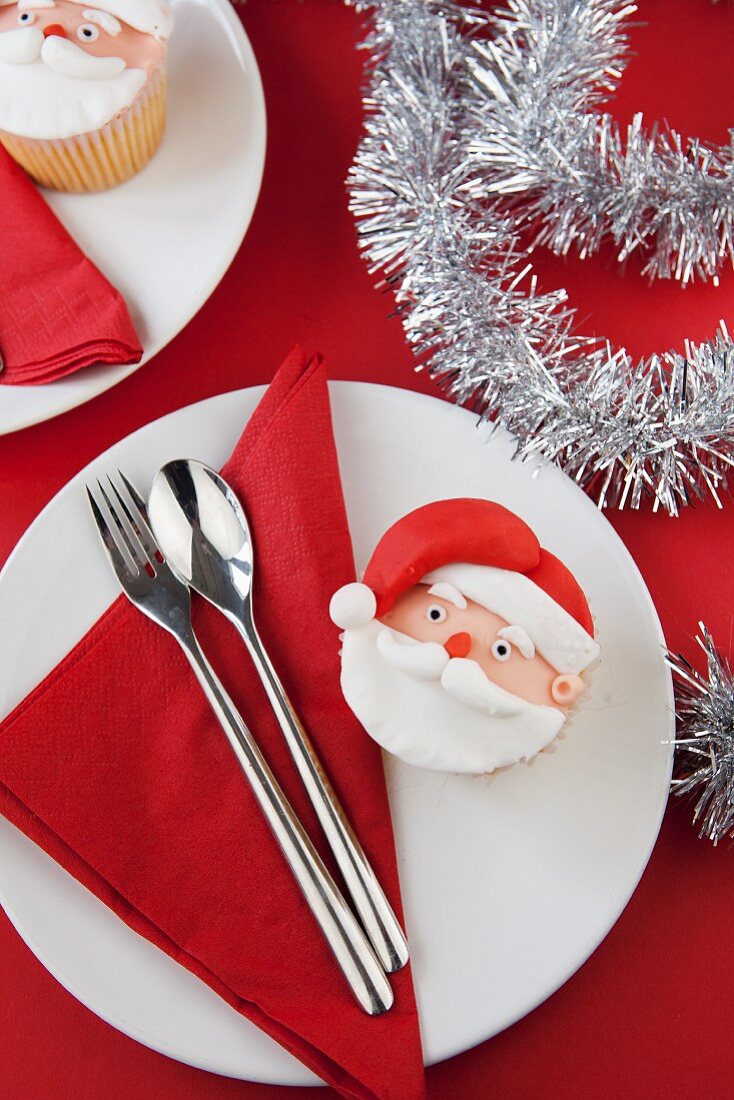 A Father Christmas cupcake on a plate with a napkin and cutlery