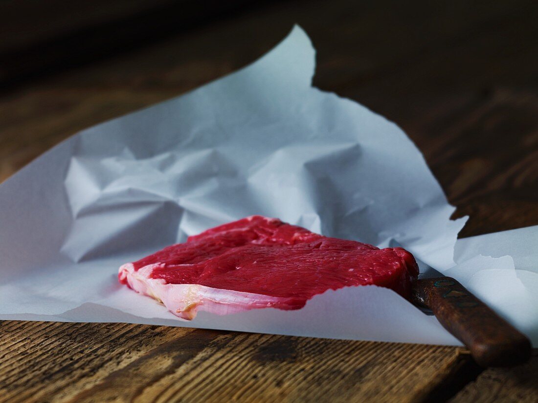 Beef steak on paper with a knife