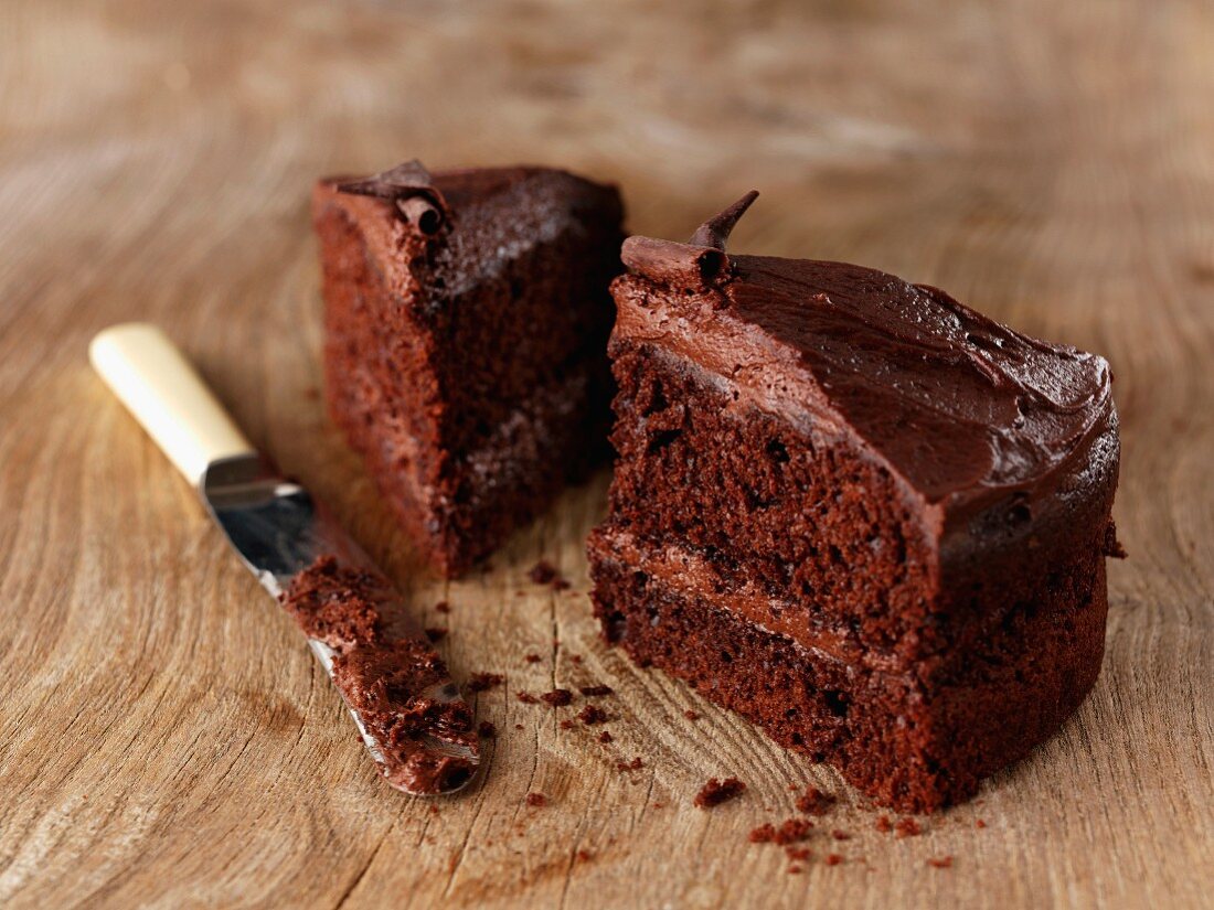Two slices of chocolate cake with a knife on a wooden surface