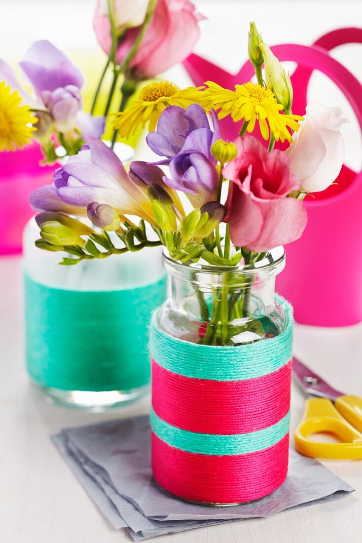 Kleine Glasflaschen mit bunten Wollgarnen umwickelt, als Blumenvase
