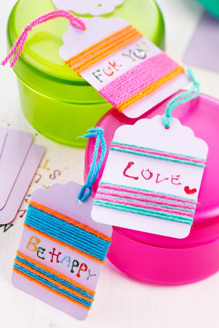 Small gift tags wrapped in colourful woollen yarn on plastic pots of different colours