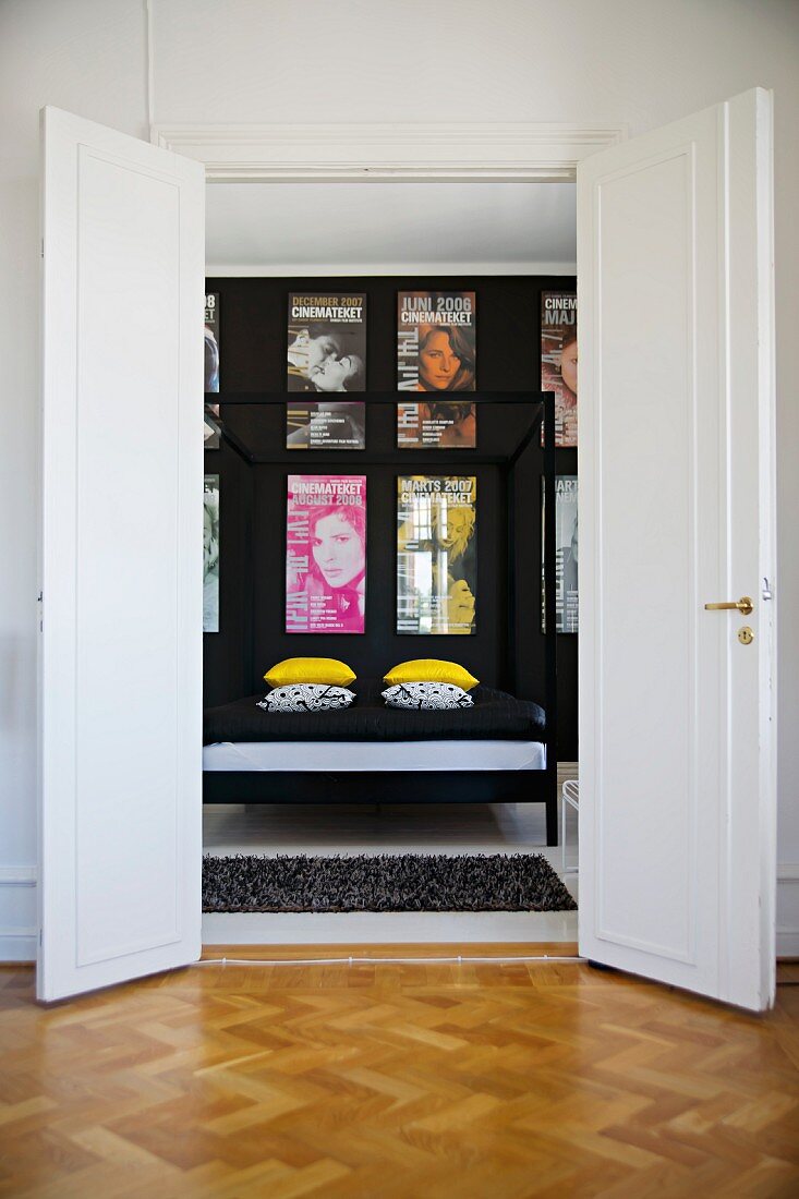 View through open double doors of four-poster bed with black metal frame and collection of posters on black wall in period apartment