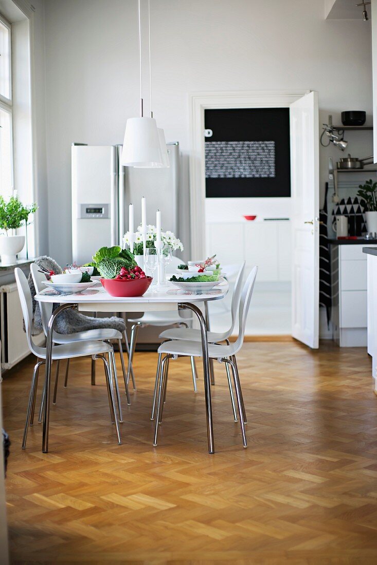 Set table and white, retro-style shell chairs in dining room with herringbone parquet floor and modern furnishings