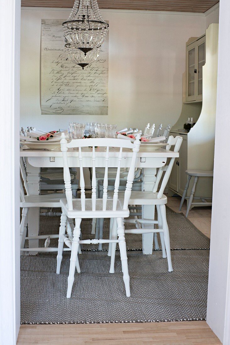 Set table and white wooden chairs in rustic dining room seen through open door