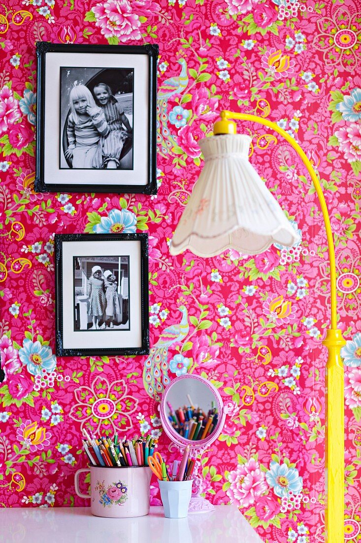Standard lamp with nostalgic fabric lampshade and yellow-painted base, framed photos on pink wallpaper with floral pattern