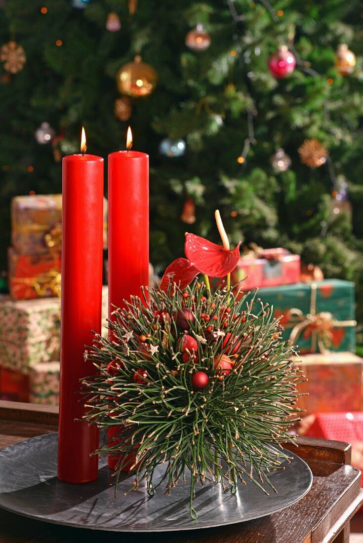 Schwebende Tannenkugel, selbstgesteckt und rote Kerzen auf Metallschale vor weihnachtlicher Deko