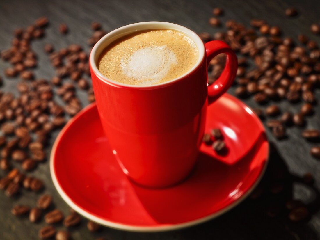 Eine Tasse Cappuccino zwischen Kaffeebohnen