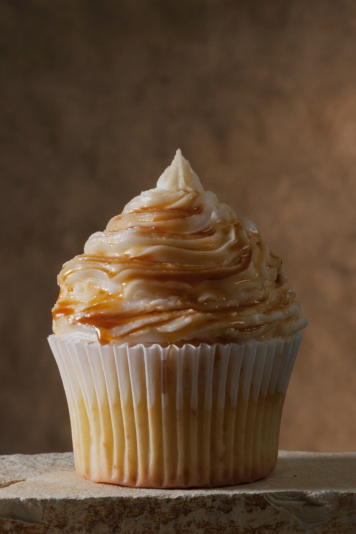 A vanilla cupcake topped with caramel icing and caramel syrup