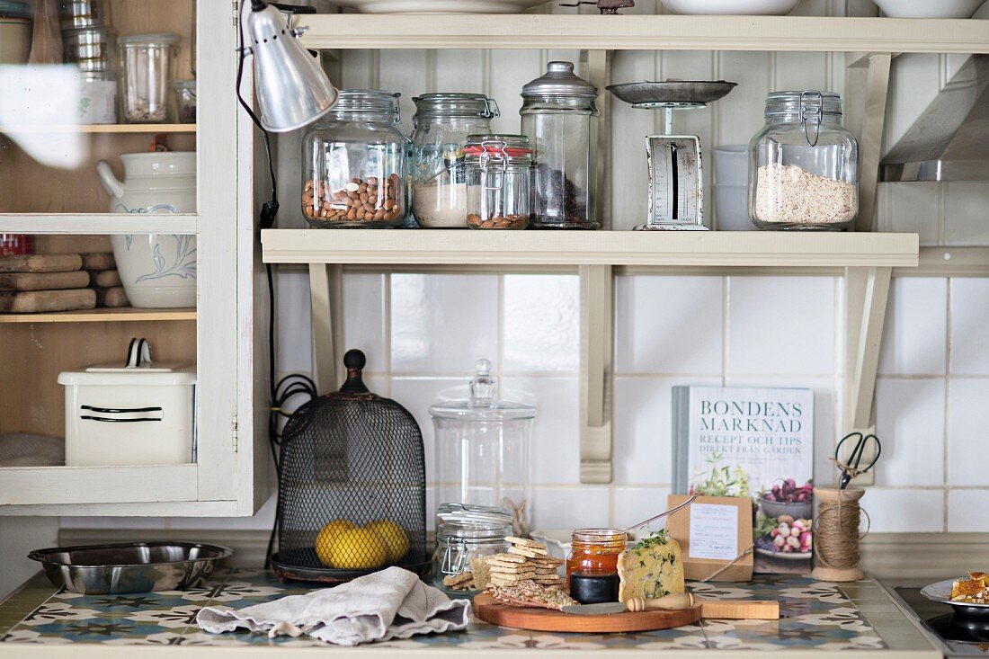 Food preparation on kitchen worksurface below storage jars on bracket shelves