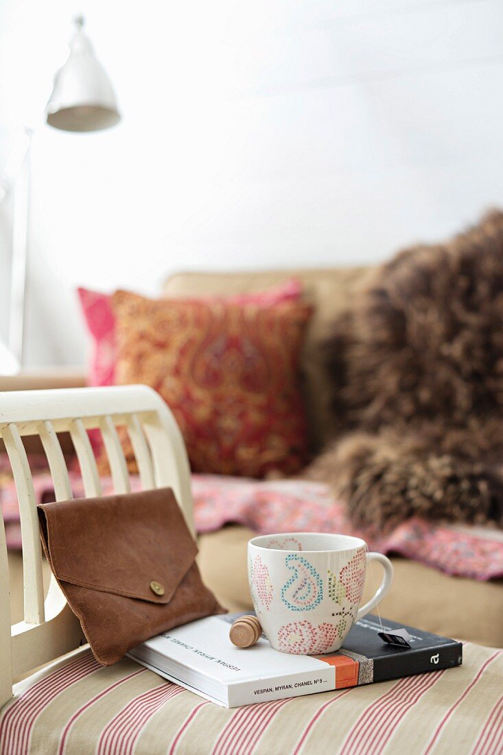 Coffee cup on book and leather clutch bag on stool with arm rest