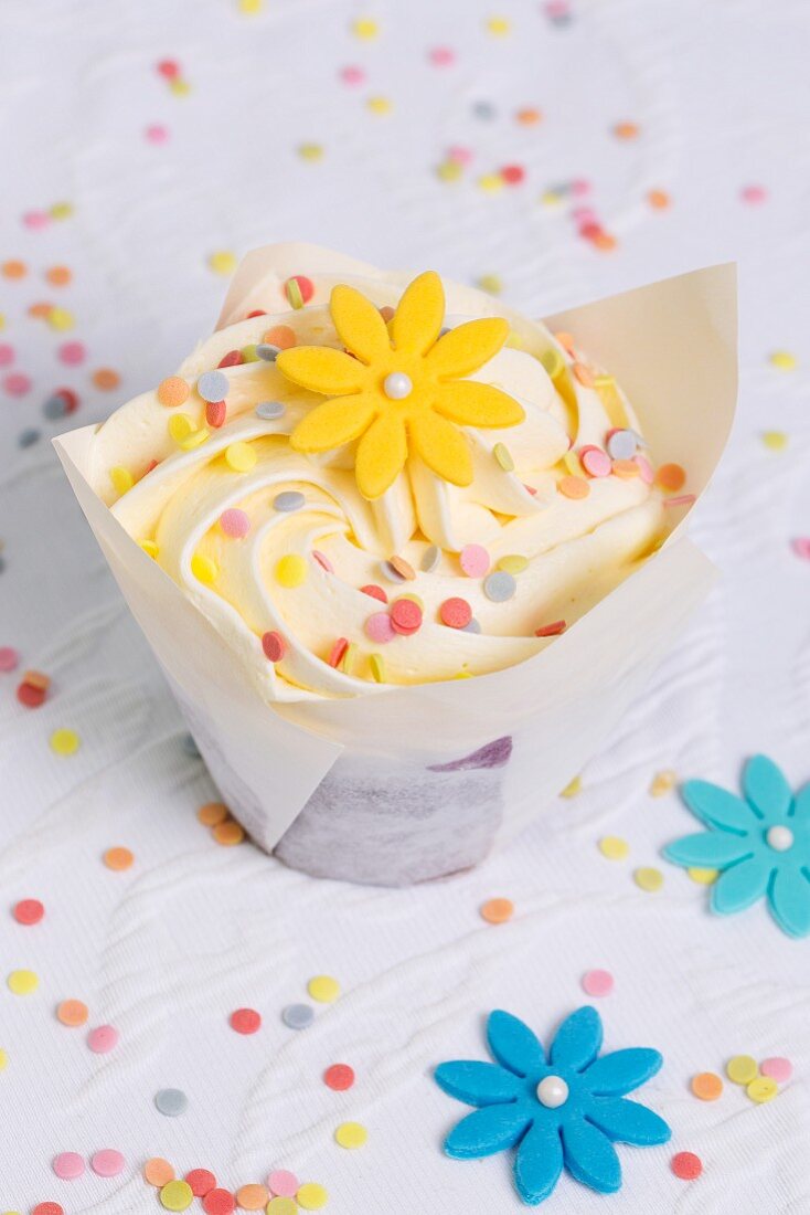 A cupcake decorated with a sugar flower and sugar confetti