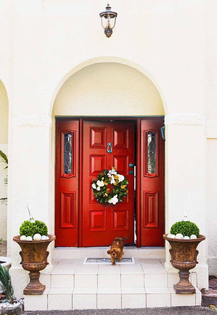 Christmas wreath on red panelled wooden door of villa with planted urns on front steps
