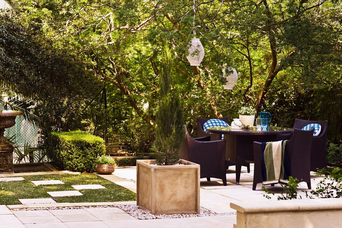 Garden furniture and cypresses in planters on paved area in sunny garden of old villa