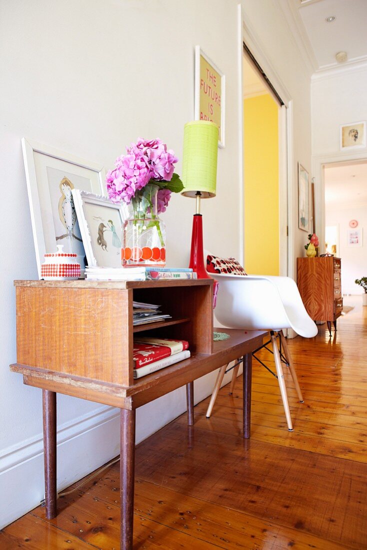 Simple wooden console table with bouquet and table lamp next to Bauhaus shell chair on wooden floor in hallway