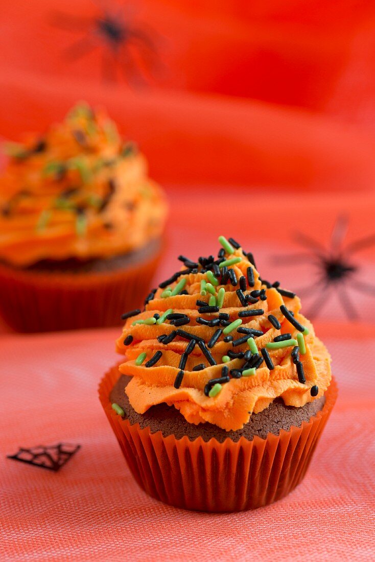 Schokoladencupcake mit orangefarbener Buttercreme und Zuckerstreuseln für Halloween