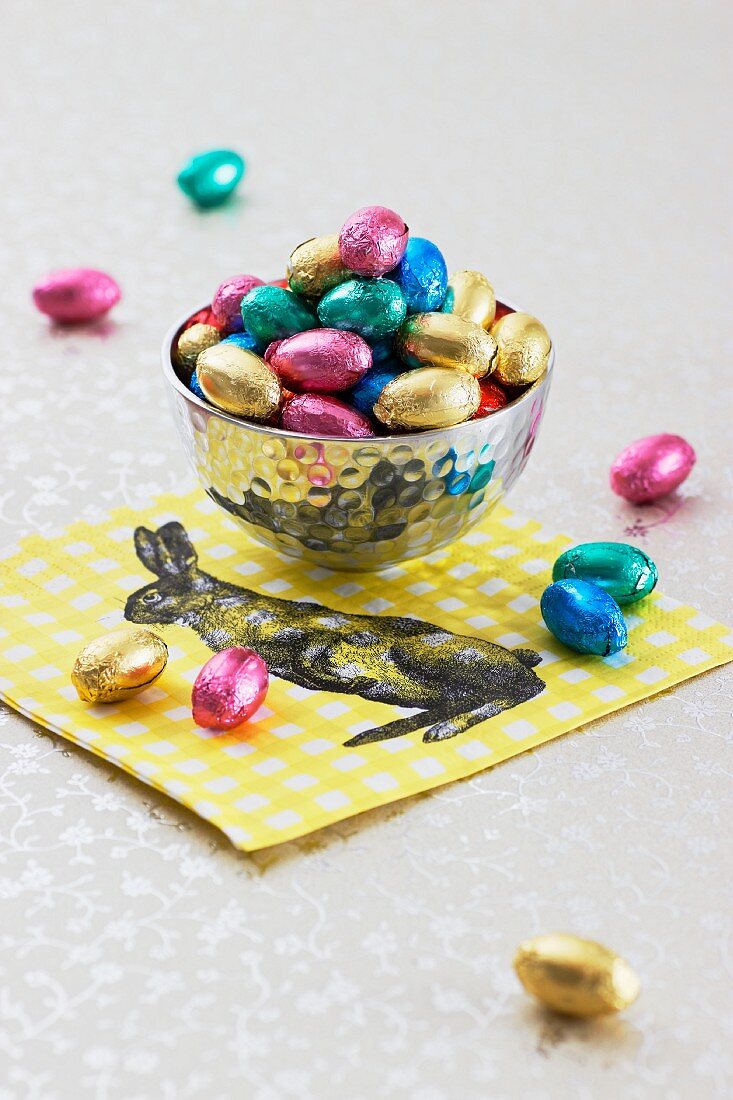 Chocolate eggs in a silver bowl on a napkin decorated with an Easter bunny