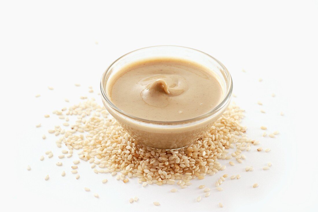 A bowl of tahini surrounded by sesame seeds