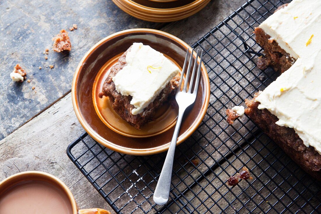 Carrot cake with an orange and cream cheese frosting with a slice on a plate