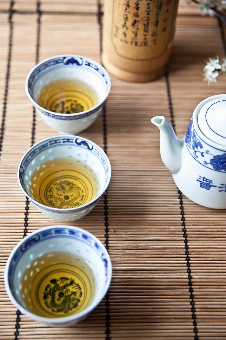 Three oriental tea bowls filled with green tea on a bamboo mat