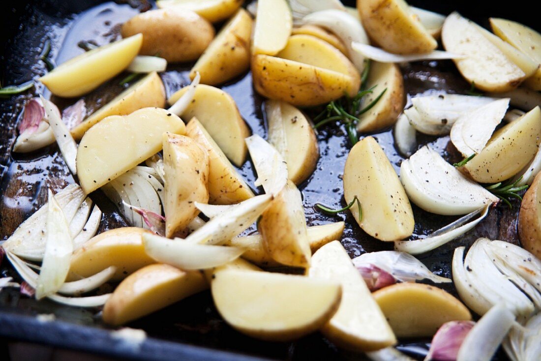 Rohe Kartoffelschnitze mit Zwiebeln, Knoblauch und Rosmarin auf Backblech