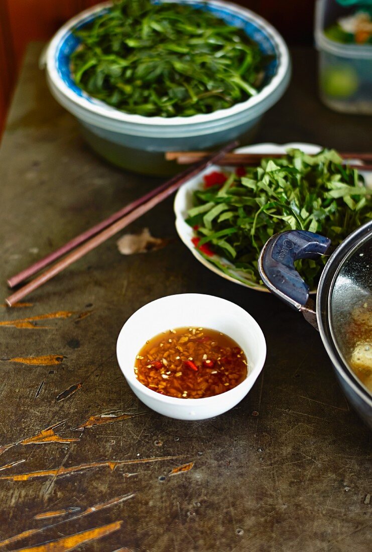 Chilisauce in Schälchen vor Blattgemüse, Vietnam