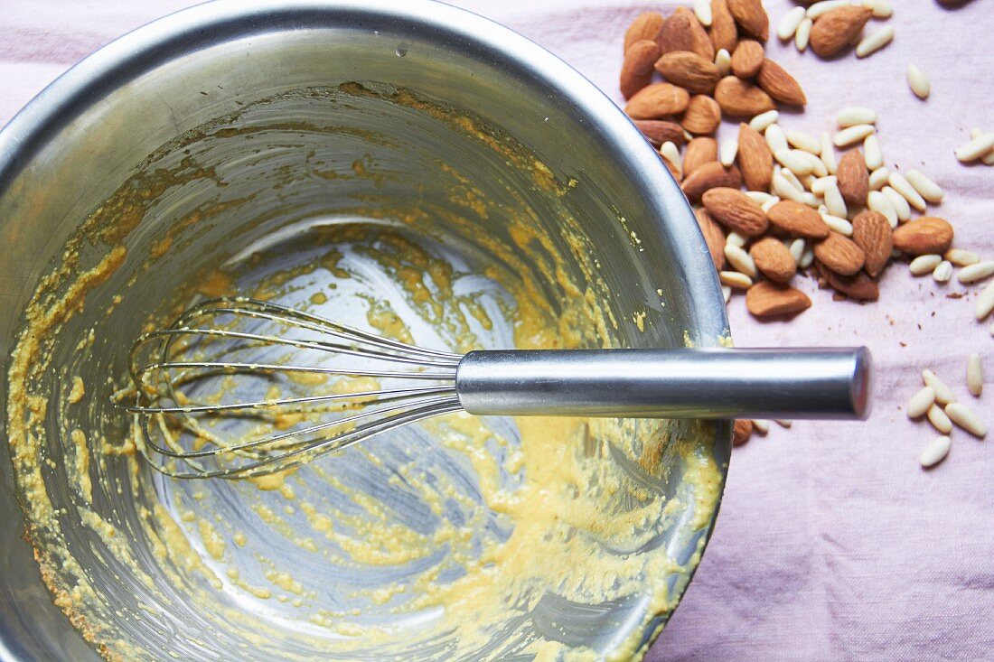 Remains of cake mixture in a bowl with almonds and pine nuts next to it