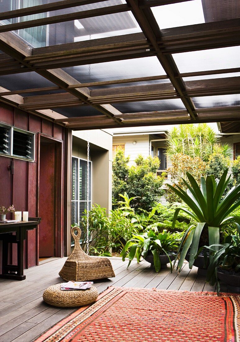 Folkloristischer Teppich und verschiedene Sitzmöbel aus Rattan, daneben tropische Pflanzen im Topf auf überdachter Terrasse