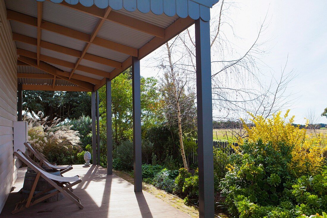 Wooden deckchairs on roofed terrace with wide view across summery garden in rural setting