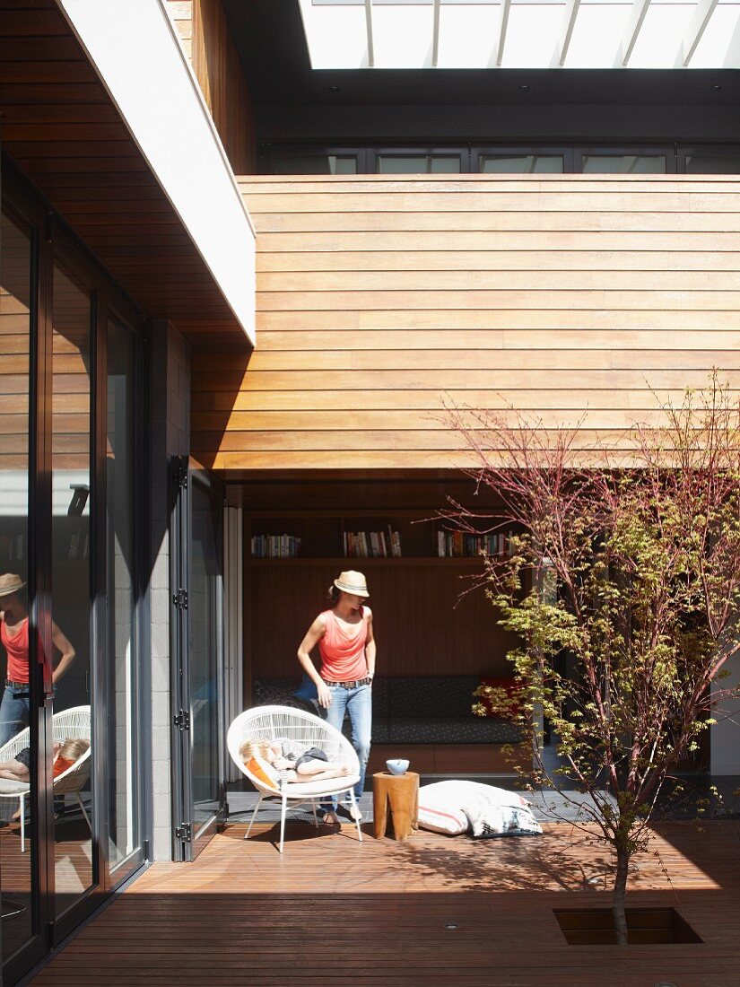 Junge Frau auf sonniger Terrasse mit Schalenstuhl und Beistellhocker