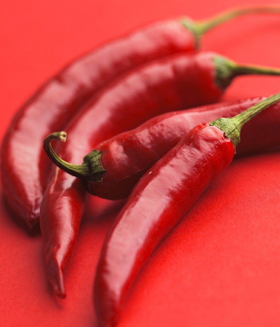 Four red chilli peppers on a red surface