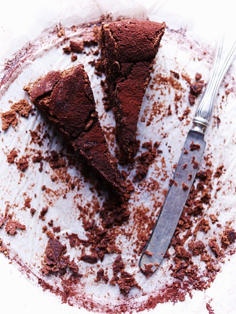 Zwei Stücke Schokoladenkuchen, Kuchenkrümel und Messer auf Kuchenplatte