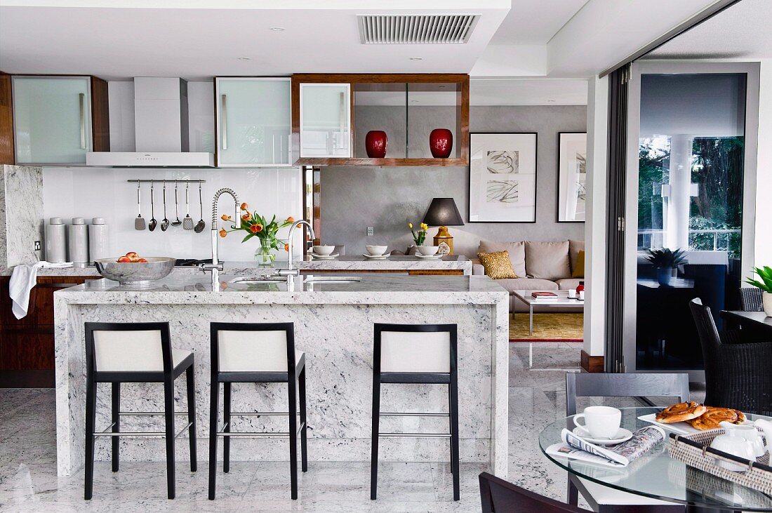 Elegant designer interior with open-plan kitchen, bar stools with black wooden frames and marble counter