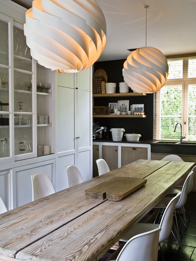 Eames chairs around robust dining table below designer lamps