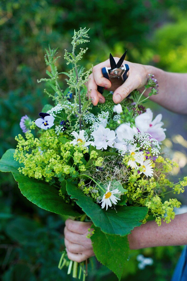 Frauenhände halten Sommerstrauss und Gartenschere