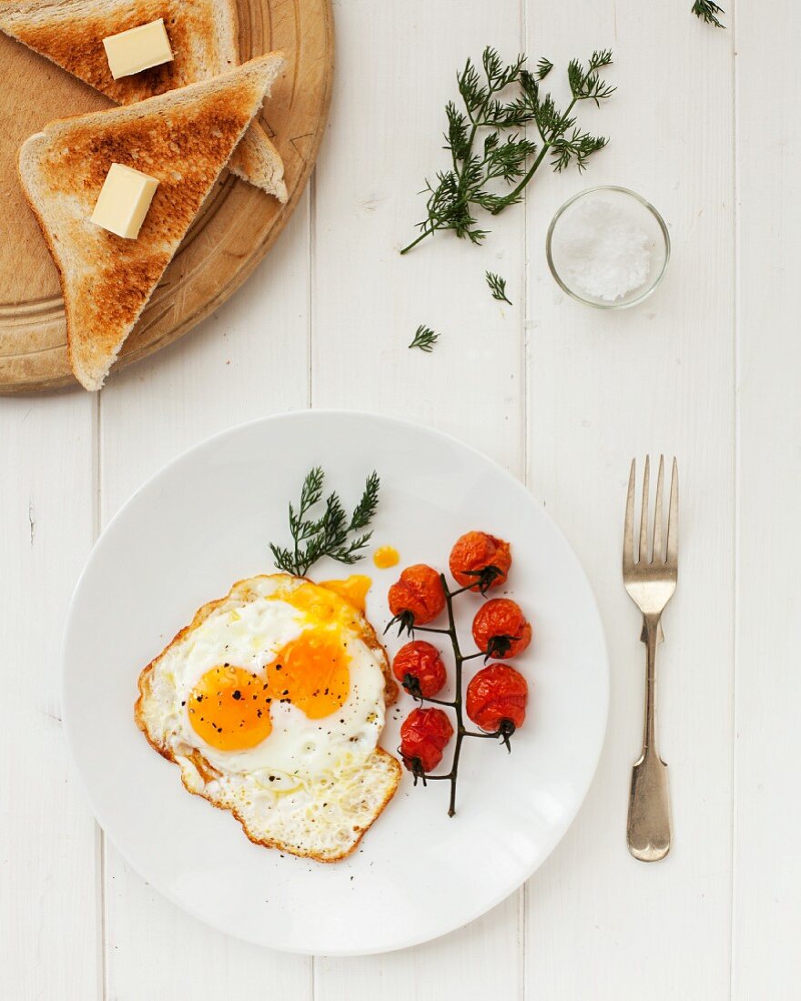 A fried egg with tomatoes and toast triangle with butter
