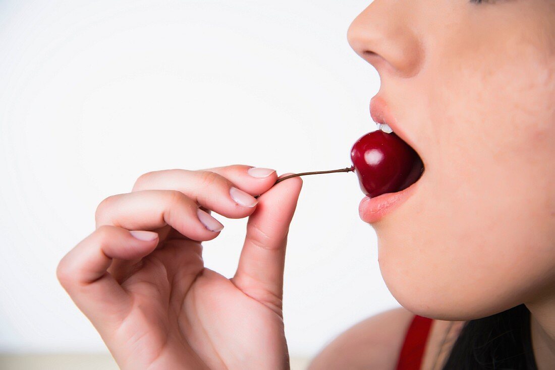 A young woman eating a cherry
