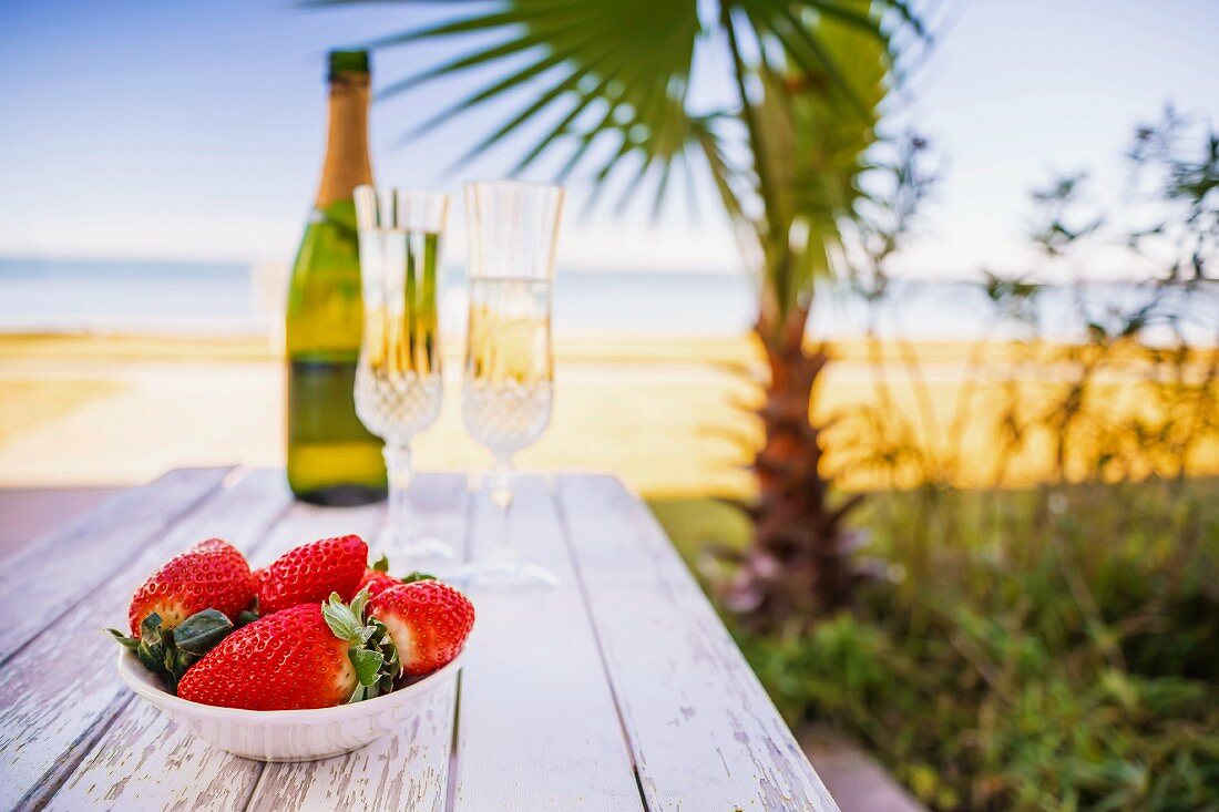 Schale mit Erdbeeren und Champagner am Strand