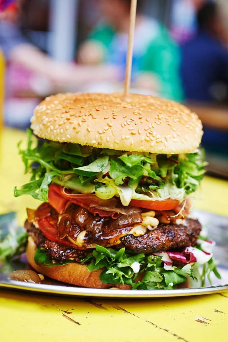 A steak burger with bacon, vegetables and lettuce