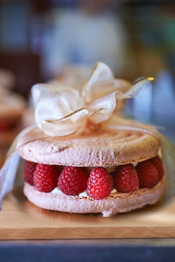 A macaroon cake with raspberries tied with a ribbon