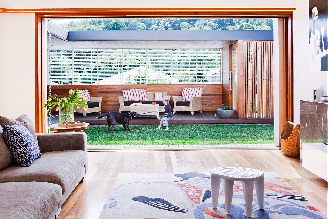 View across sofa and patterned rug through open sliding doors of table and chairs on roofed outdoor living room