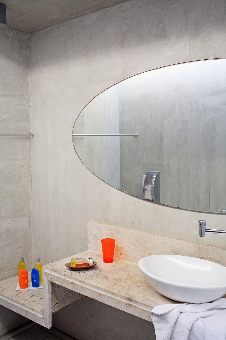 Washstand with white china basin on stepped concrete surface and oval mirror on concrete wall