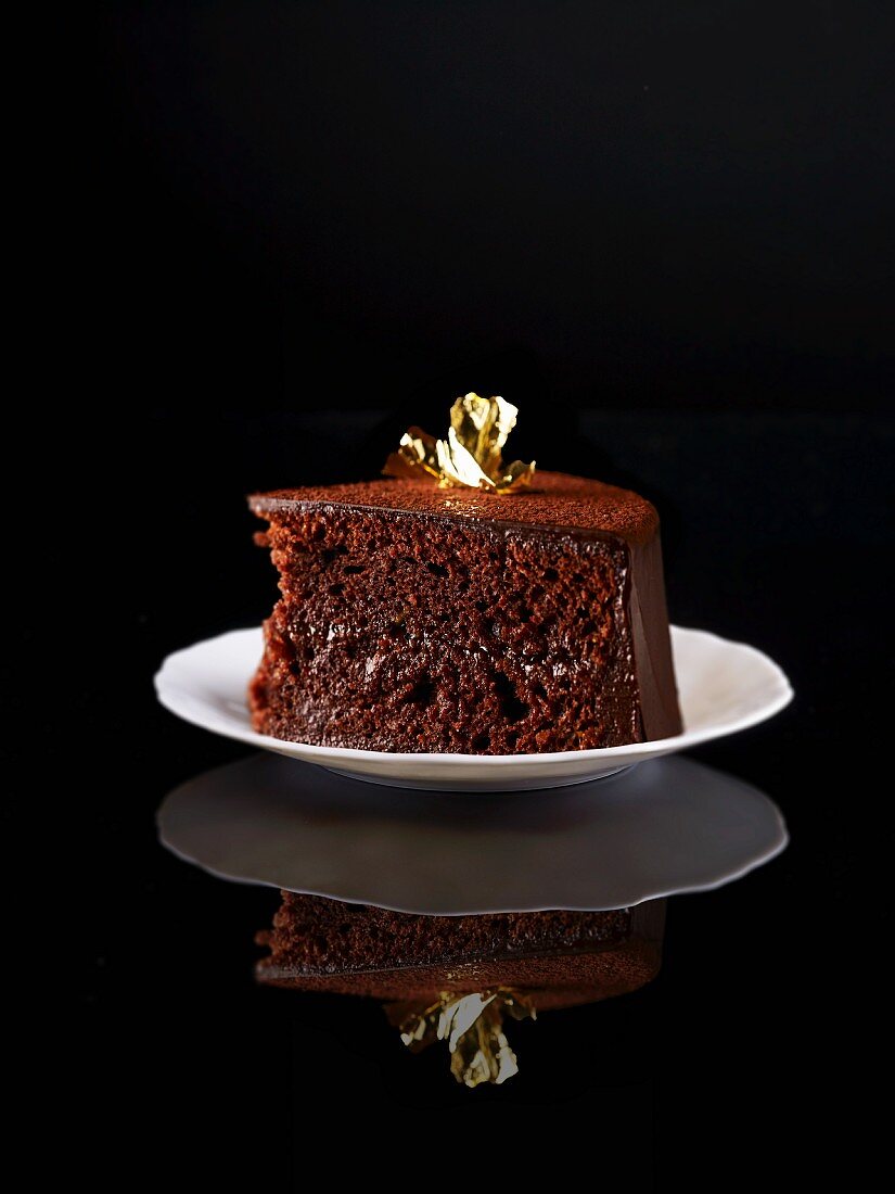 A slice of Sachertorte (rich Austrian chocolate cake) decorated with gold leaf on a plate