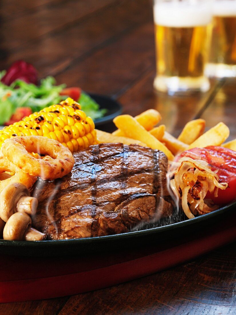 Grilled beefsteak with corn on the cob, mushrooms, onion rings and chips