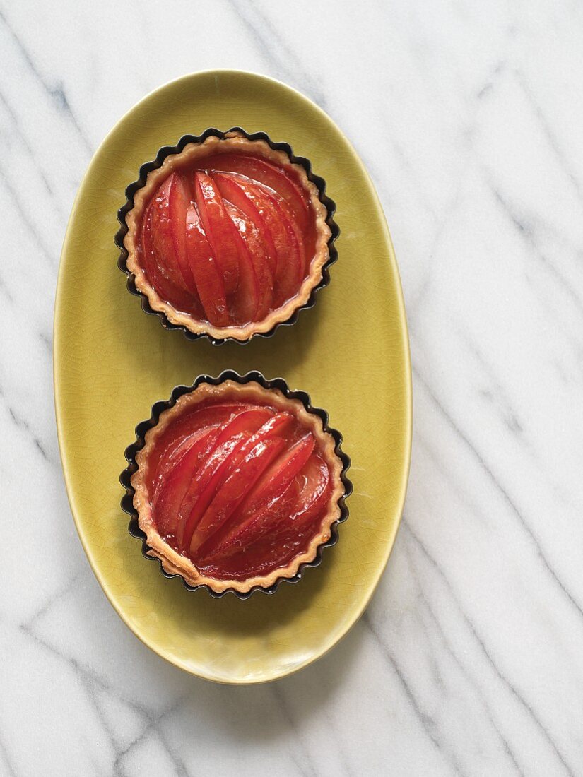 Two gluten-free plum Tarts in ramekins on an oval plate