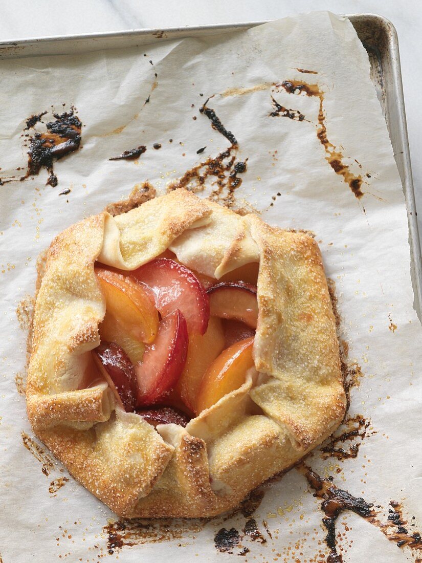 A peach and plum tart on a baking tray lined with paper